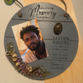 Round hanging memorial plaque with slate gray finish, photo slot, engraved name and dates, dried wildflowers, and cremated remains resin orb