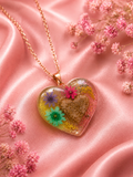 Heart-shaped resin memorial necklace with pressed wildflowers in pink, purple and teal, gold flakes, and cremated remains on a rose gold chain